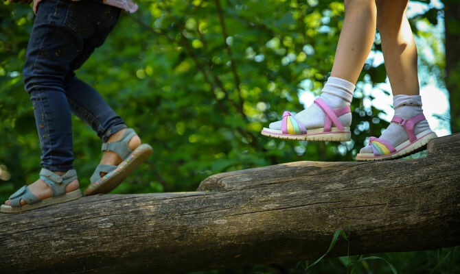 Mehrere Kinderfüße balancieren in Sandalen - mit und ohne Socken - über einen Baumstamm